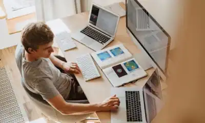 Laptops e computadores em um ambiente de trabalho moderno com múltiplas telas e dispositivos digitais.