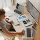 Laptops e computadores em um ambiente de trabalho moderno com múltiplas telas e dispositivos digitais.