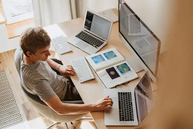 Laptops e computadores em um ambiente de trabalho moderno com múltiplas telas e dispositivos digitais.