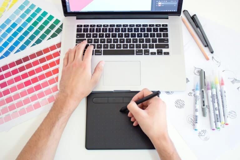 Réplica de mão de designer gráfico usando tablet digital e laptop para criar arte digital.
