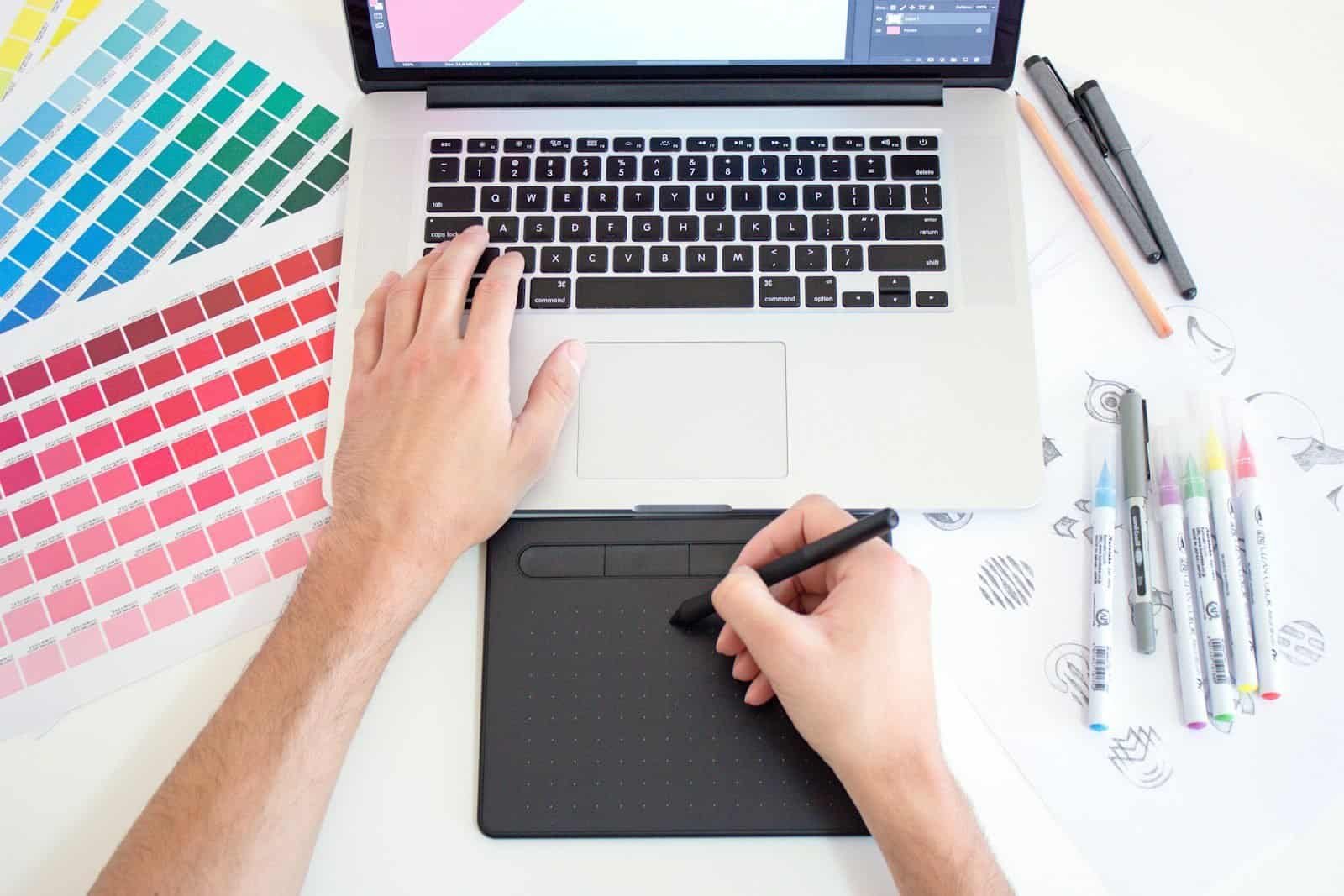 Réplica de mão de designer gráfico usando tablet digital e laptop para criar arte digital.