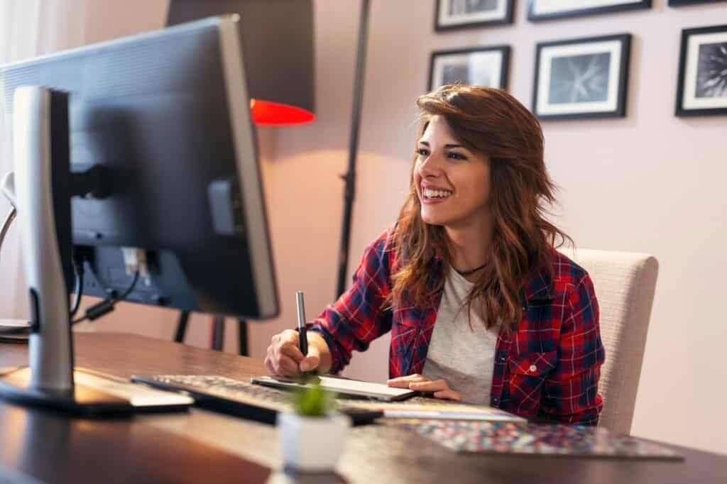 Alto_texto: Mulher trabalhando em computador com tablet e caneta em escritório moderno.