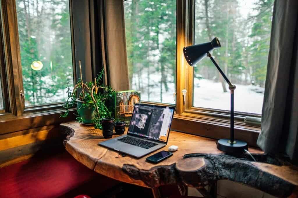 Teclado, smartphone, e macbook sobre mesa de madeira com vista para natureza de inverno.