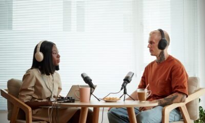 Áudio de podcast com duas pessoas conversando, usando fones de ouvido, em ambiente de estúdio.