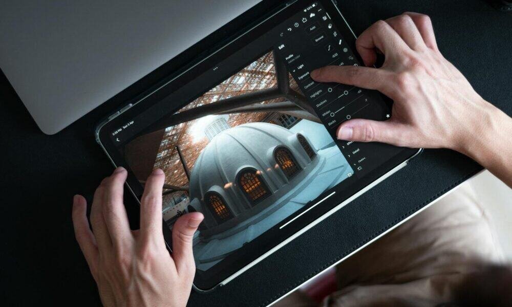 Fotografia de uma pessoa editando uma imagem em tablet com aplicativo de edição de fotos, mostrando ajustes de luz e contraste.