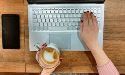 Teclado de laptop branco com uma mão segurando uma xícara de café e a outra teclado.