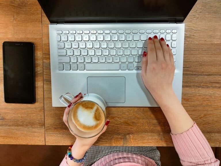 Teclado de laptop branco com uma mão segurando uma xícara de café e a outra teclado.
