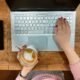 Teclado de laptop branco com uma mão segurando uma xícara de café e a outra teclado.