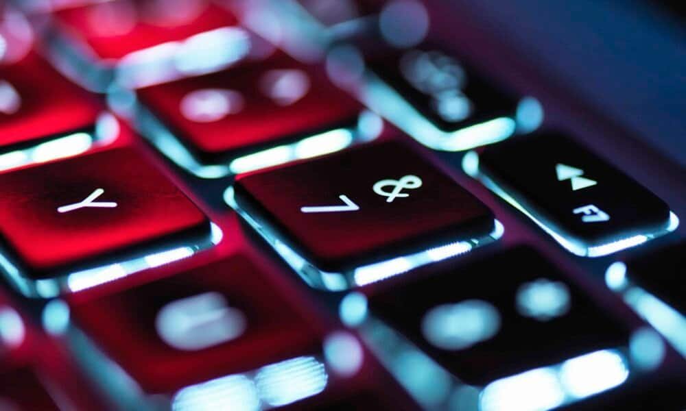 Teclado retroiluminado de laptop com luz de fundo azul e vermelho, foco em teclas de funções.