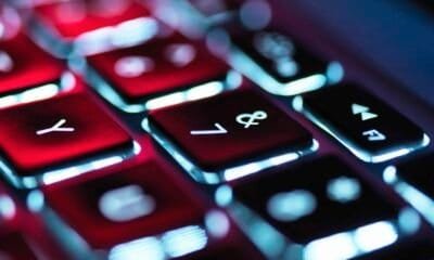 Teclado retroiluminado de laptop com luz de fundo azul e vermelho, foco em teclas de funções.