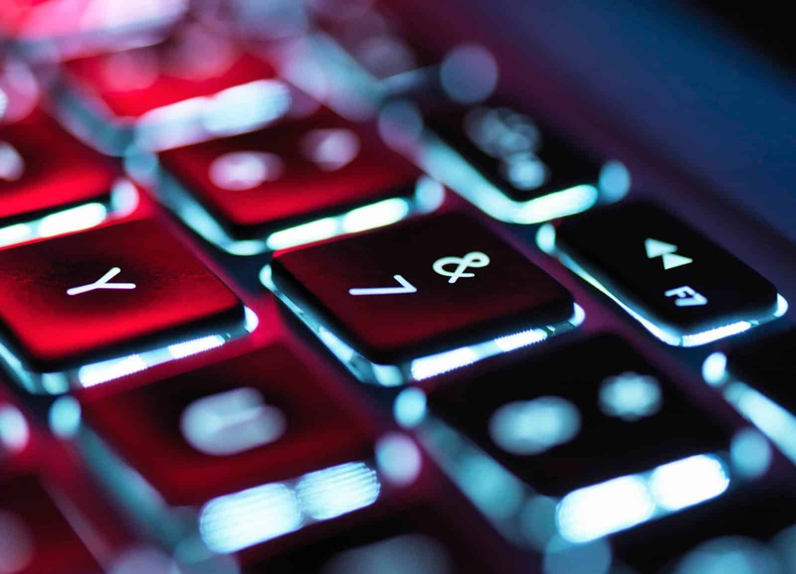 Teclado retroiluminado de laptop com luz de fundo azul e vermelho, foco em teclas de funções.