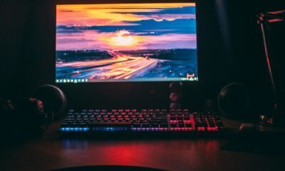 Monitor de computador com iluminação RGB, teclado gamer e fones de ouvido destacam um setup de tecnologia.