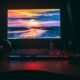 Monitor de computador com iluminação RGB, teclado gamer e fones de ouvido destacam um setup de tecnologia.