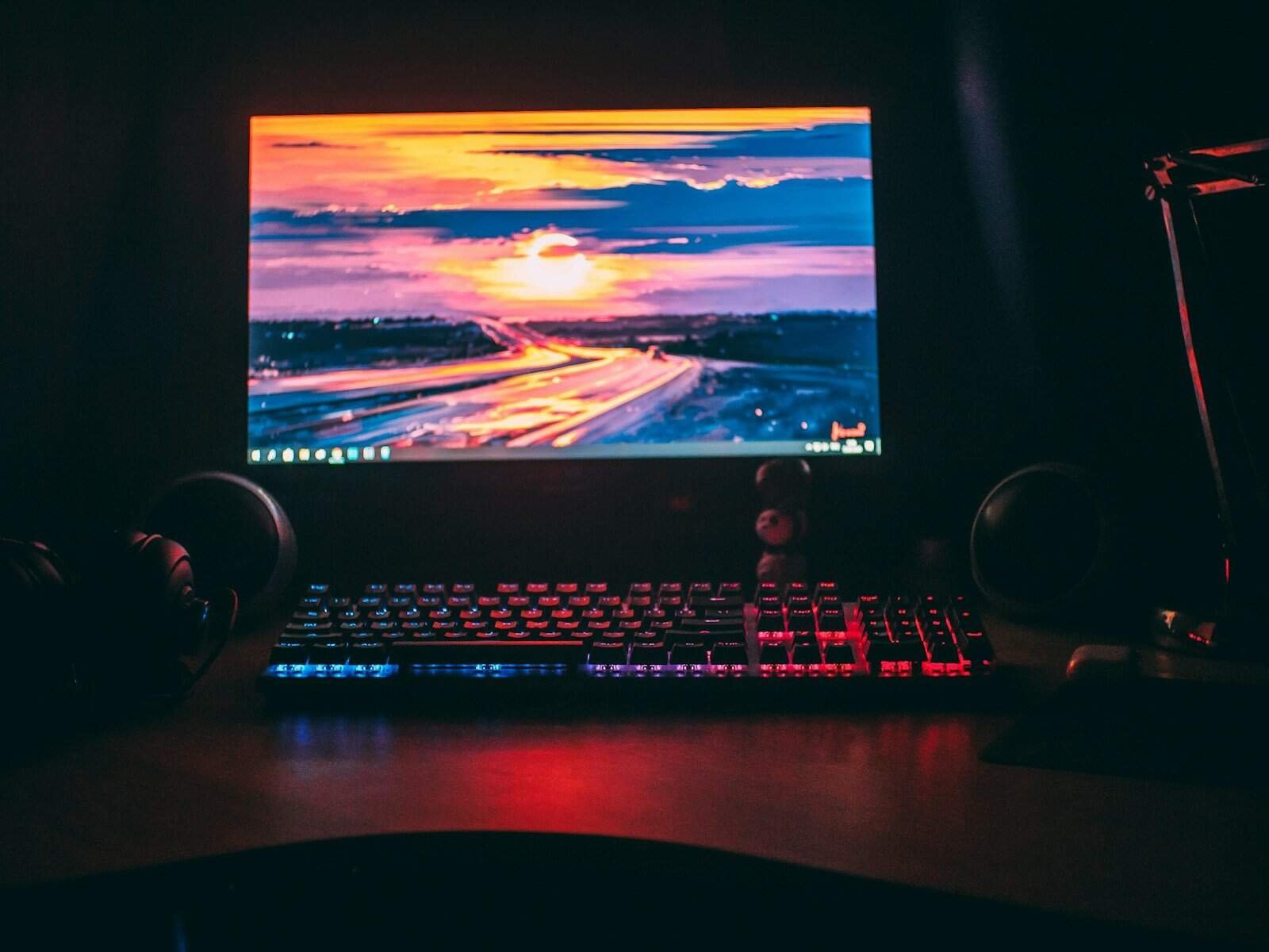 Monitor de computador com iluminação RGB, teclado gamer e fones de ouvido destacam um setup de tecnologia.