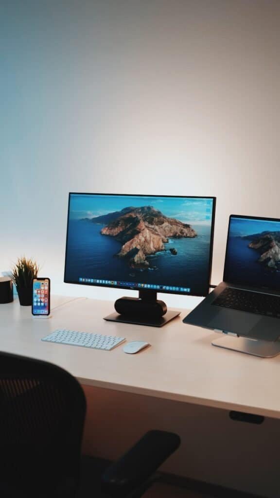 Monitor com tela de fundo de natureza em escritório de tecnologia com computador, smartphone e acessórios tecnológicos.