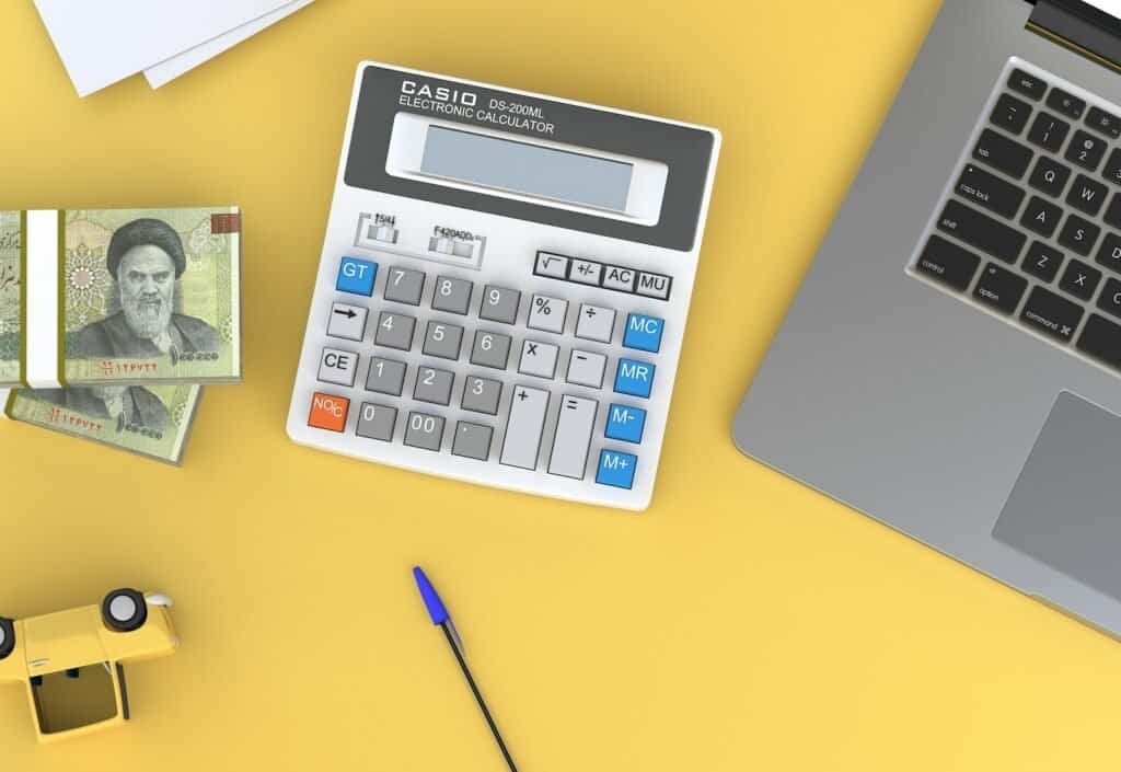 Calculadora científica de escritório com notas de dinheiro e laptop em fundo amarelo.