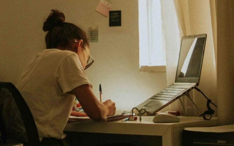 Estudante estudando em frente ao computador em casa, foco em tecnologia e educação online.