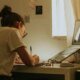 Estudante estudando em frente ao computador em casa, foco em tecnologia e educação online.