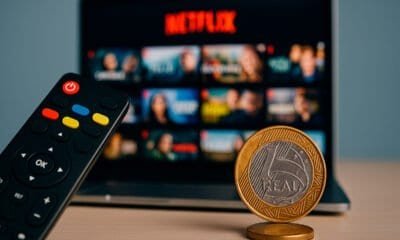 Netflix na TV com controle remoto e moeda de 1 real sobre mesa.