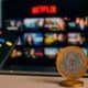 Netflix na TV com controle remoto e moeda de 1 real sobre mesa.