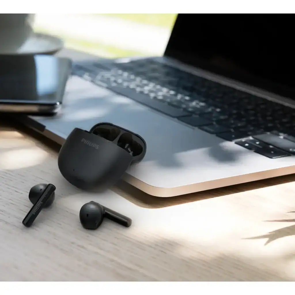 Fones de ouvido wireless com estojo na mesa de trabalho, laptop e ambiente de escritório.