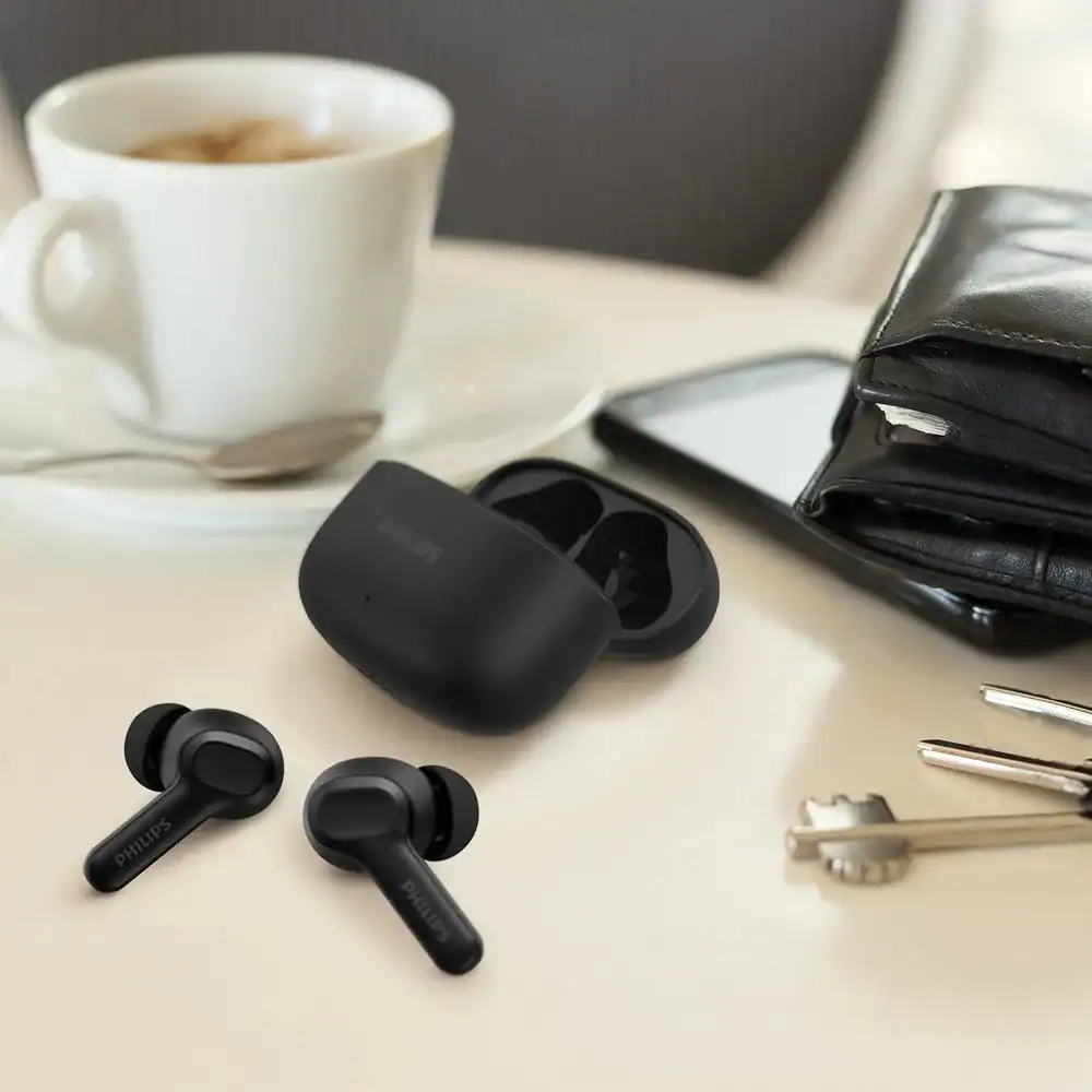 Fones de ouvido sem fio Philips com estojo de carregamento e smartphone em mesa de trabalho.