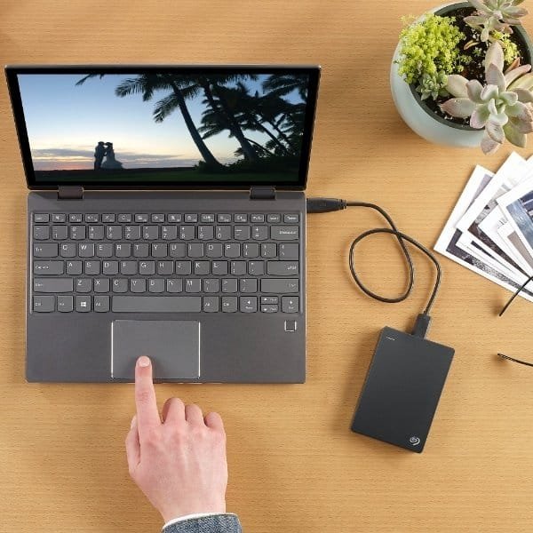 Notebook conectado a unidade externa de armazenamento, com plantas e revistas ao redor.