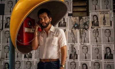 Telefone público antigo em taça, estilo retrô, com fundo de posters políticos preto e branco.