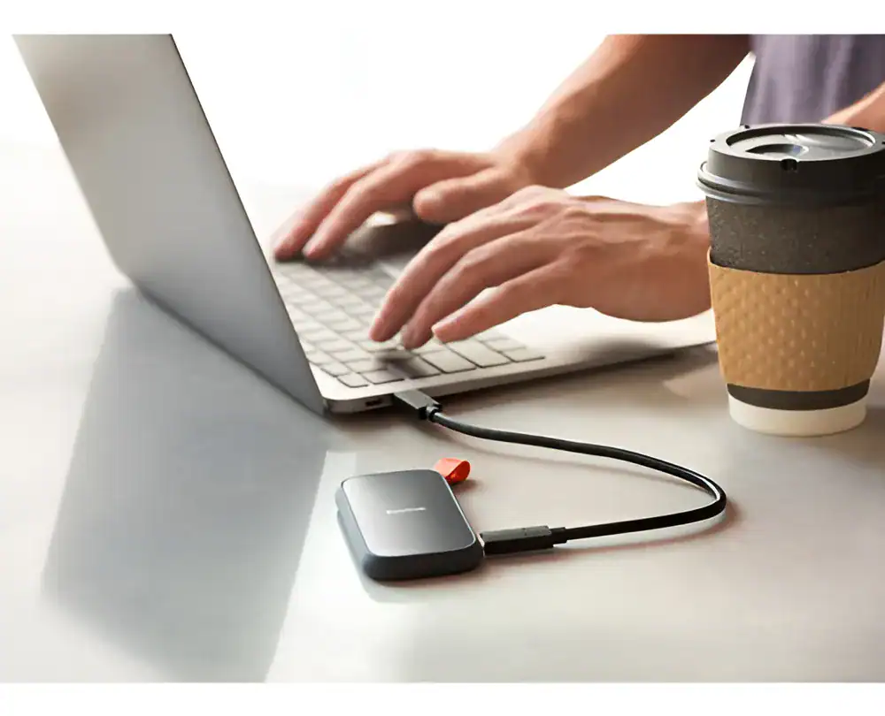 Carregador portátil conectado ao laptop com uma xícara de café ao lado.