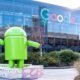 Android em frente ao prédio do Google, símbolo de tecnologia e inovação.