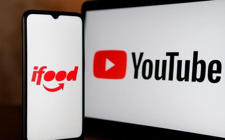 Ifood app na tela do celular e logo do YouTube na tela do monitor.