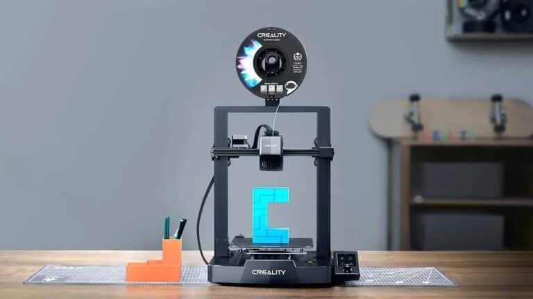 Impressora 3D Criality criando objeto de plástico azul em uma mesa de trabalho.