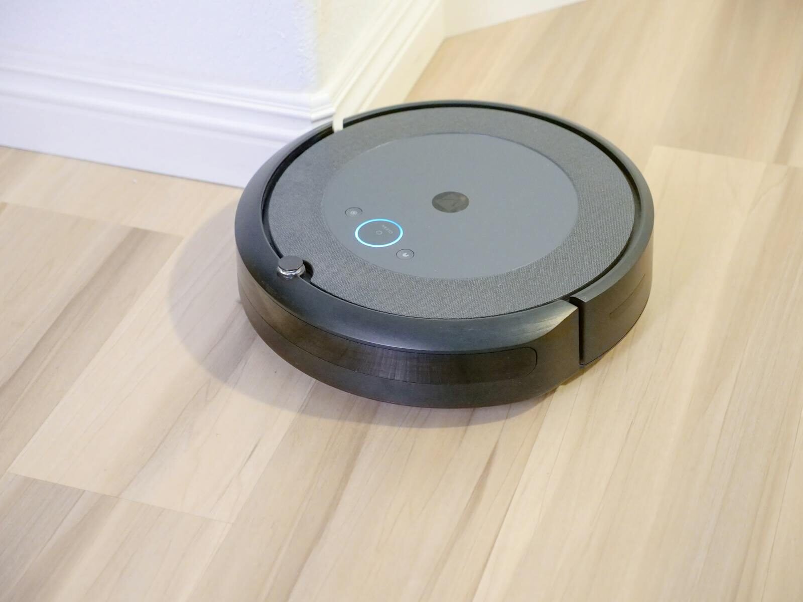 Robô aspirador de pó preto em piso de madeira, tecnologia de limpeza automatizada.
