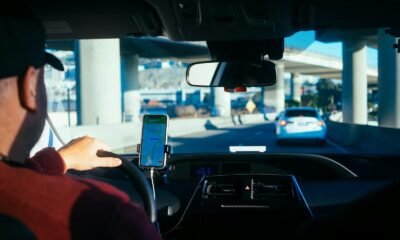 Pessoa usando smartphone no carro, tecnologia de condução autônoma em destaque.