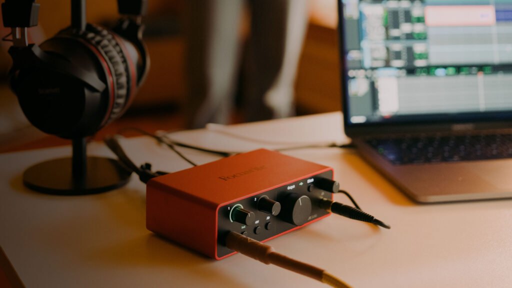 Interface de áudio vermelha com controles, fones de ouvido e laptop com software de edição musica.