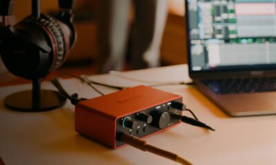 Interface de áudio vermelha com controles, fones de ouvido e laptop com software de edição musica.