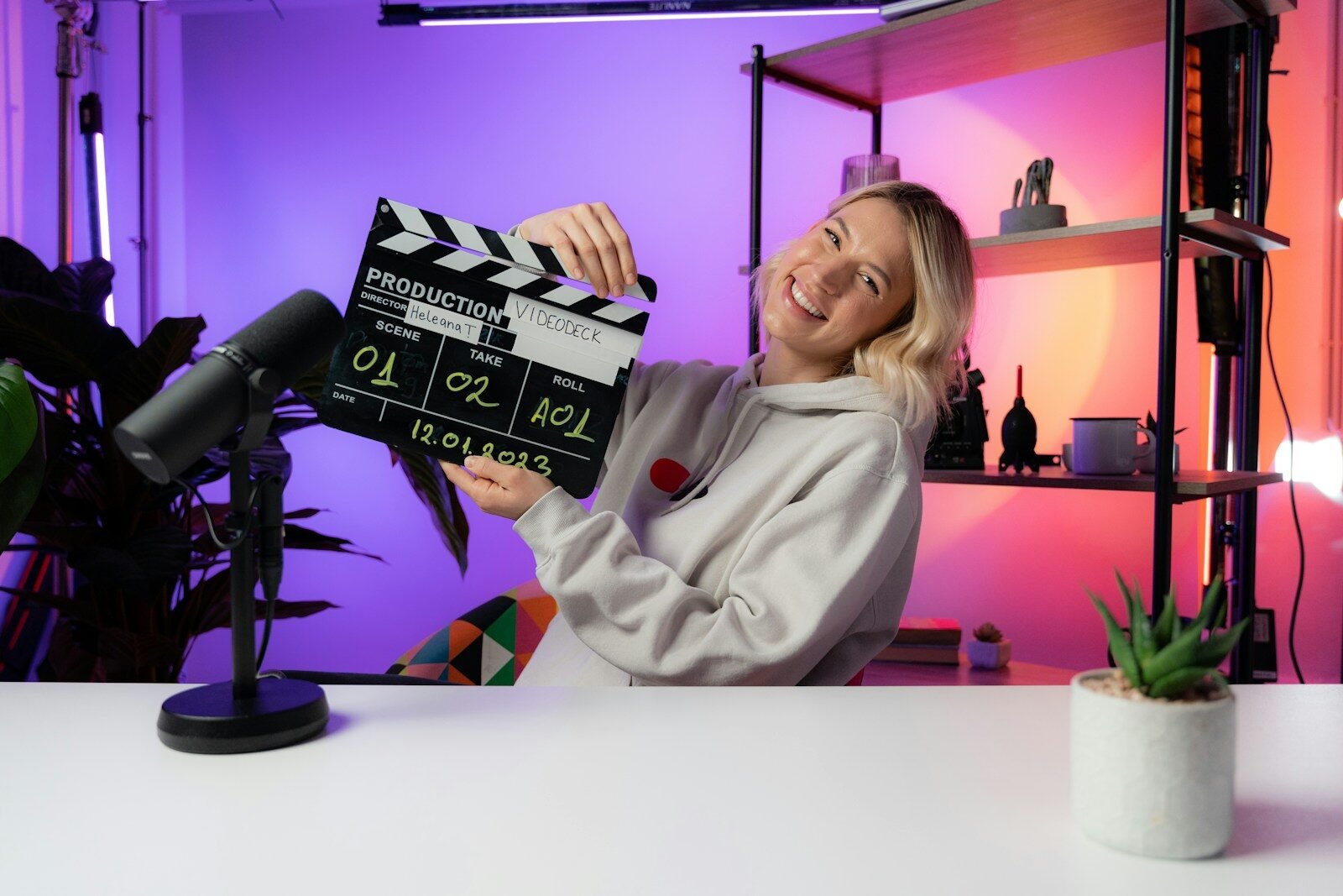 Imagem de uma mulher sorridente segurando uma claquete de produção de vídeo em um ambiente de estúdi.