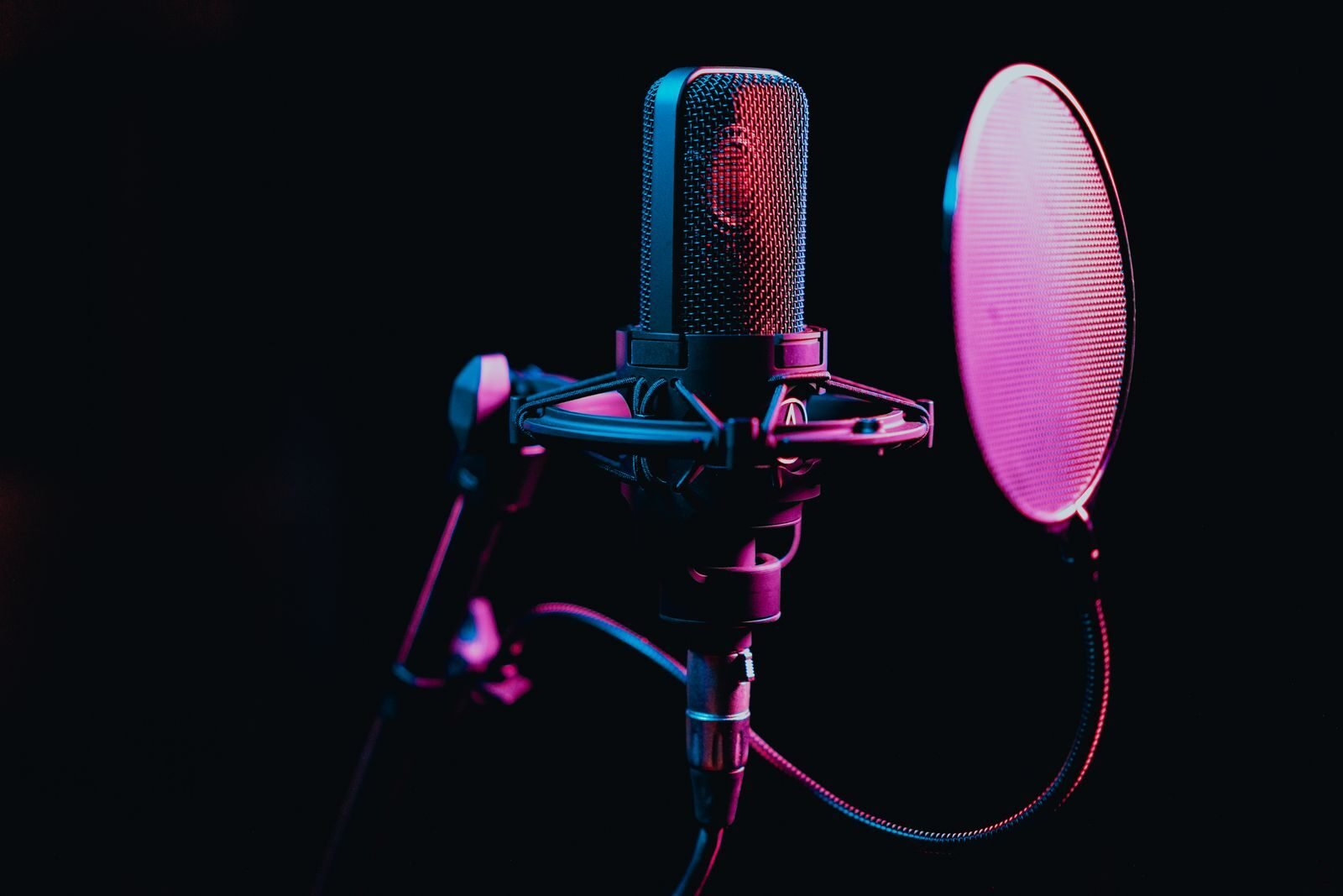 Close-up image of a condenser microphone with a pop filter in a studio setting, featuring atmospheric lighting.